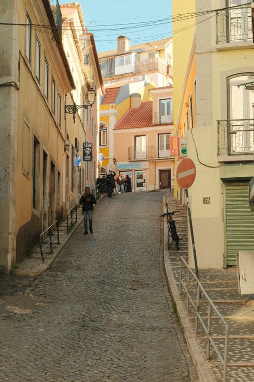 Free Explore a picturesque cobblestone street in Lisbon with vibrant buildings and urban charm. Stock Photo