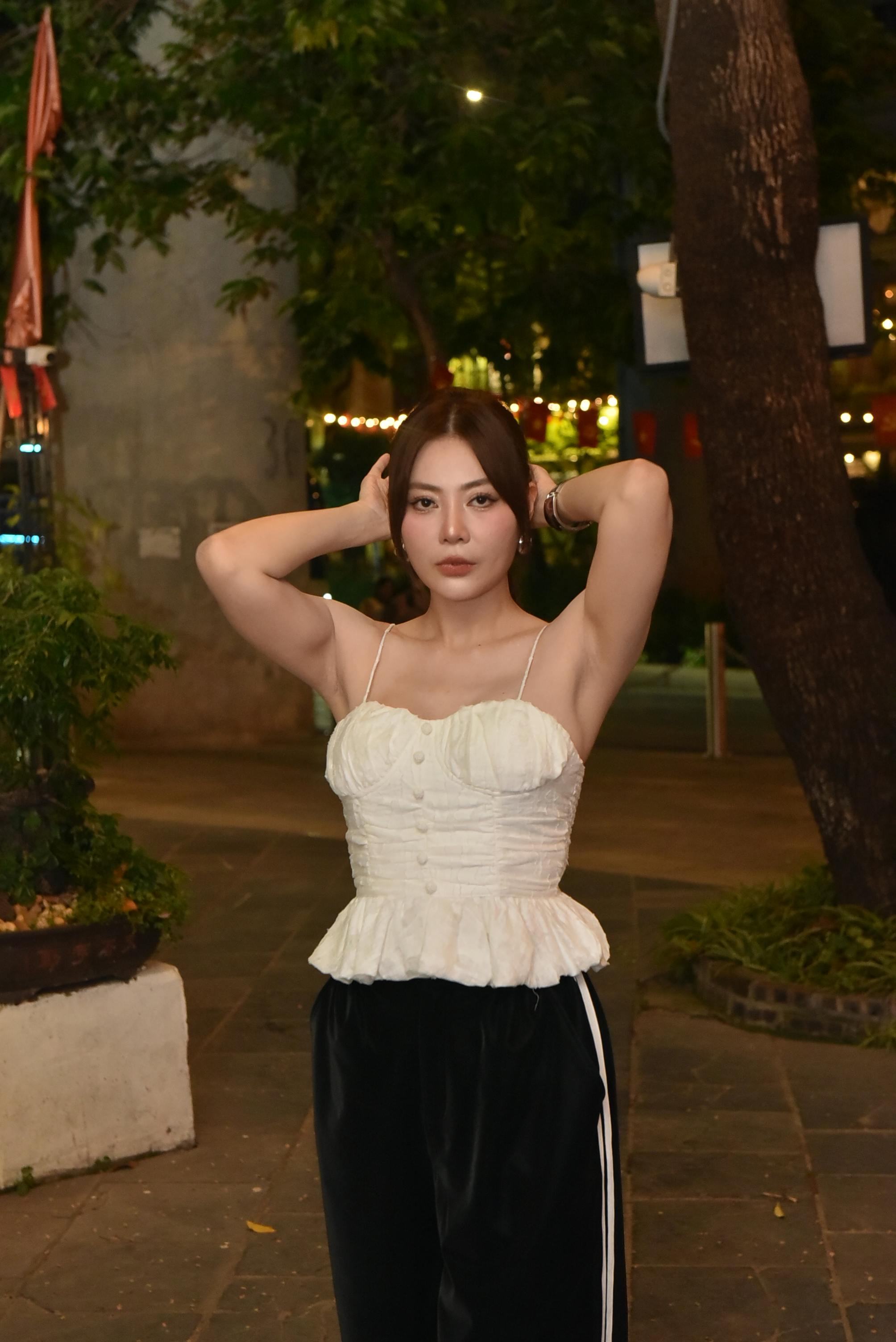 grátis Uma jovem de blusa branca posa com confiança ao ar livre à noite, com luzes ambientes que criam uma atmosfera acolhedora. Foto profissional