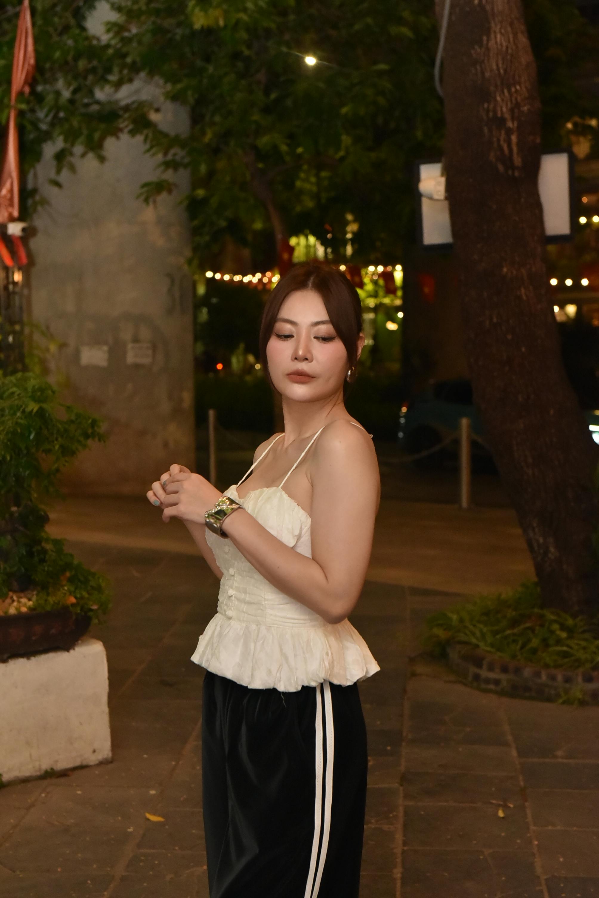 grátis Mulher elegante com blusa branca posa ao ar livre à noite, cercada por luzes urbanas. Foto profissional