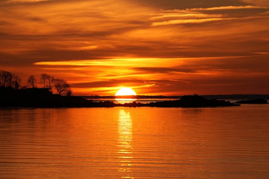 Stunning sunset casting vibrant orange hues over a peaceful lake, reflecting a tranquil evening atmosphere.