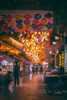 A vibrant display of traditional lanterns illuminates a bustling street market in Chongqing at night.