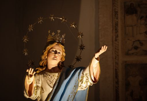 Close-up of a decorative religious statue with a starry halo inside a church, emphasized by warm lighting.