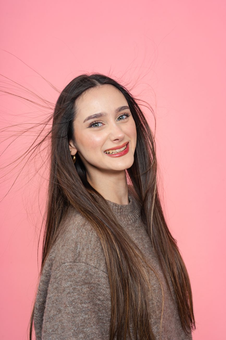 Portrait of a smiling young woman with long hair against a pink backdrop, conveying warmth and positivity.