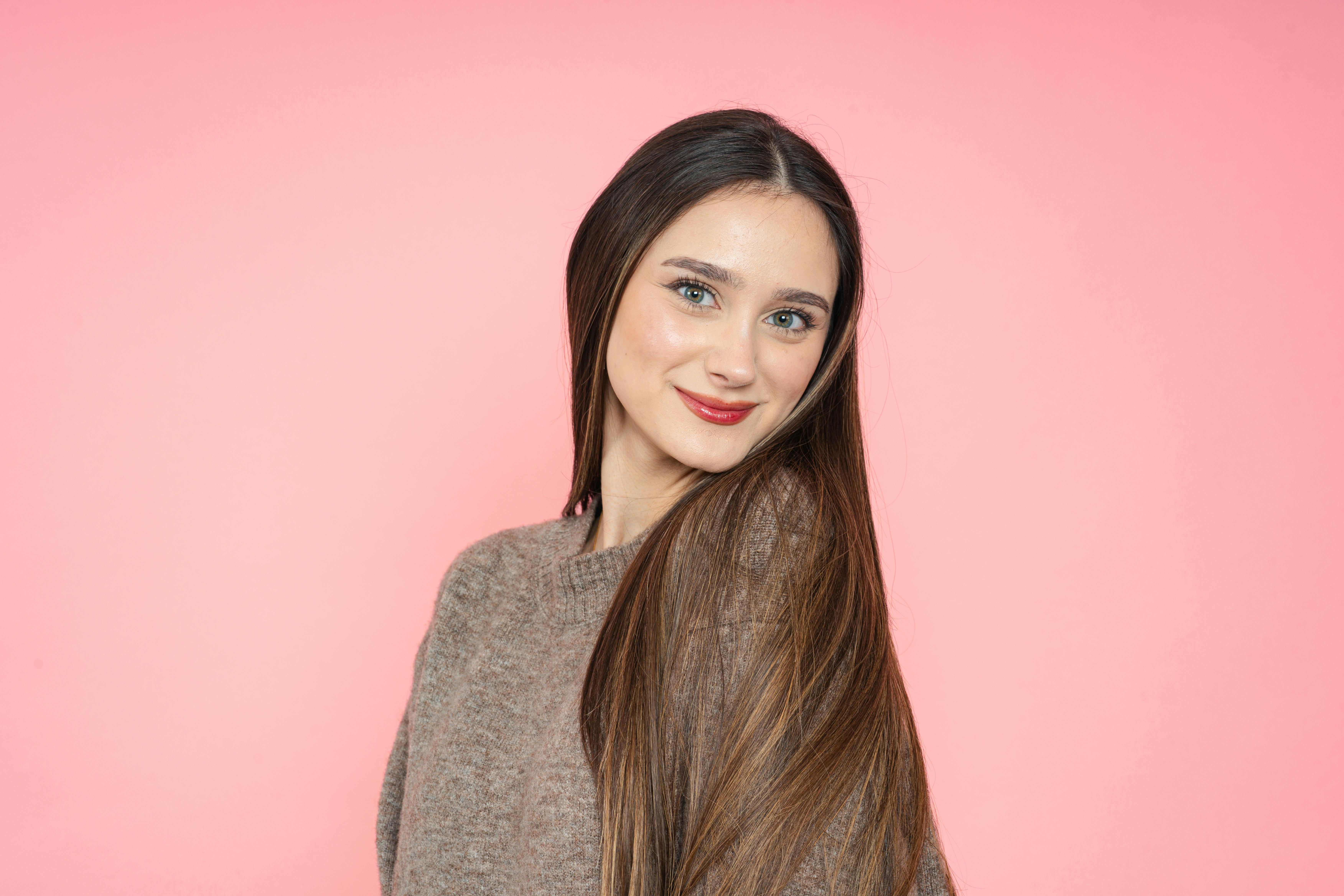 De franc Retrat d'una dona jove somrient amb els cabells llargs i castanys sobre un fons rosa. Foto d'estoc