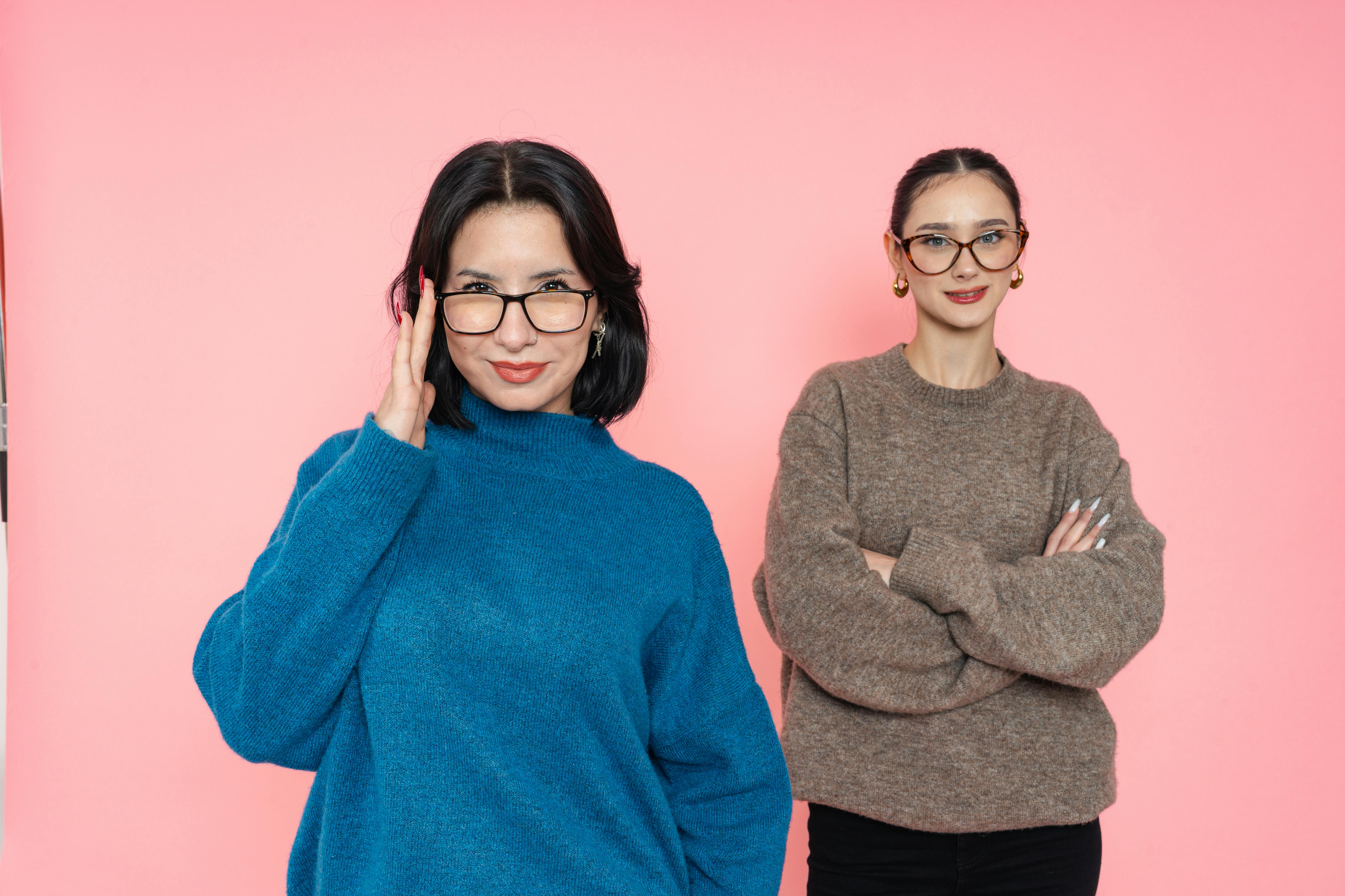 De franc Dues dones elegants amb ulleres posen amb confiança sobre un fons rosa. Foto d'estoc