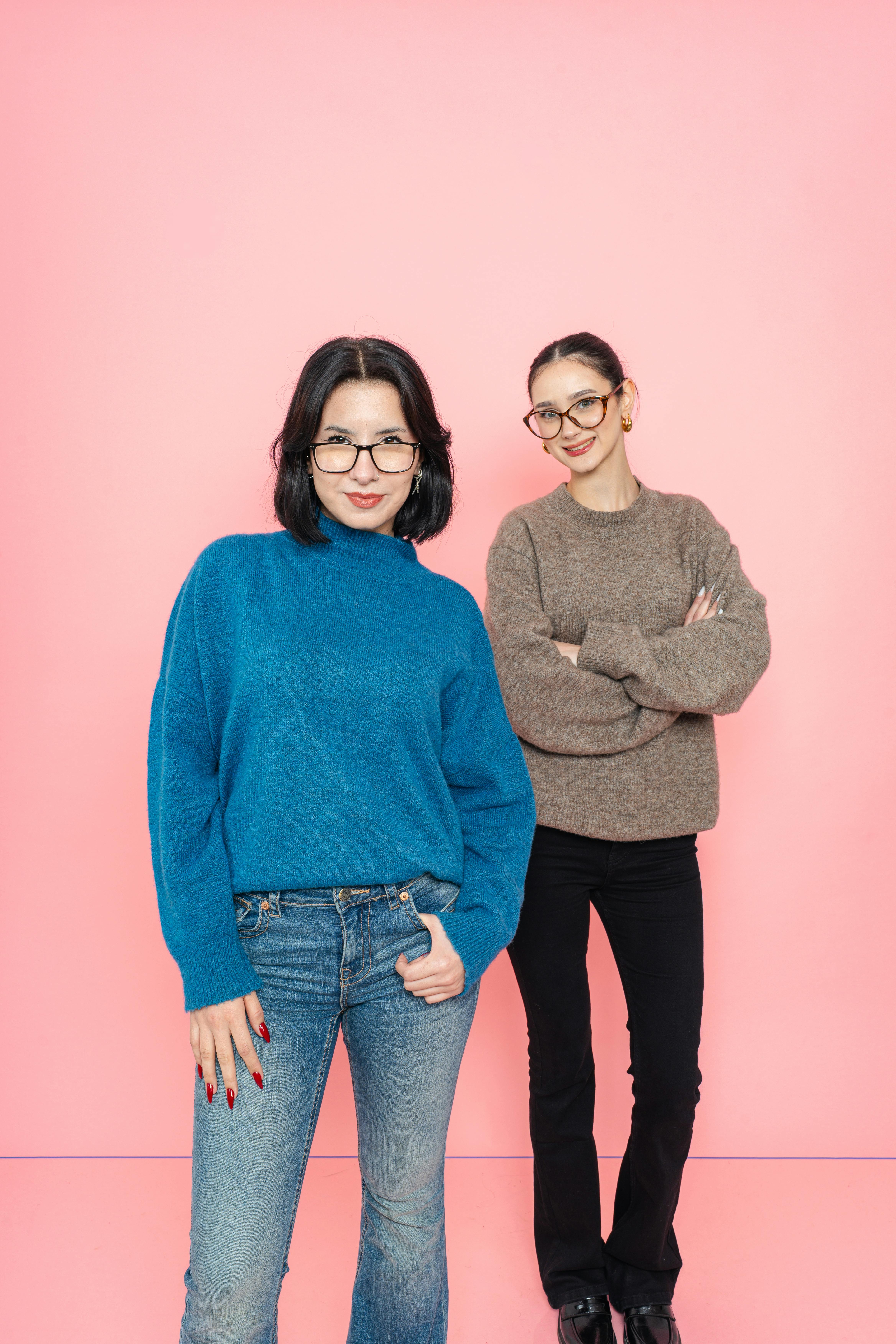 De franc Dues dones posen amb confiança amb jerseis informals sobre un fons rosa vibrant. Foto d'estoc