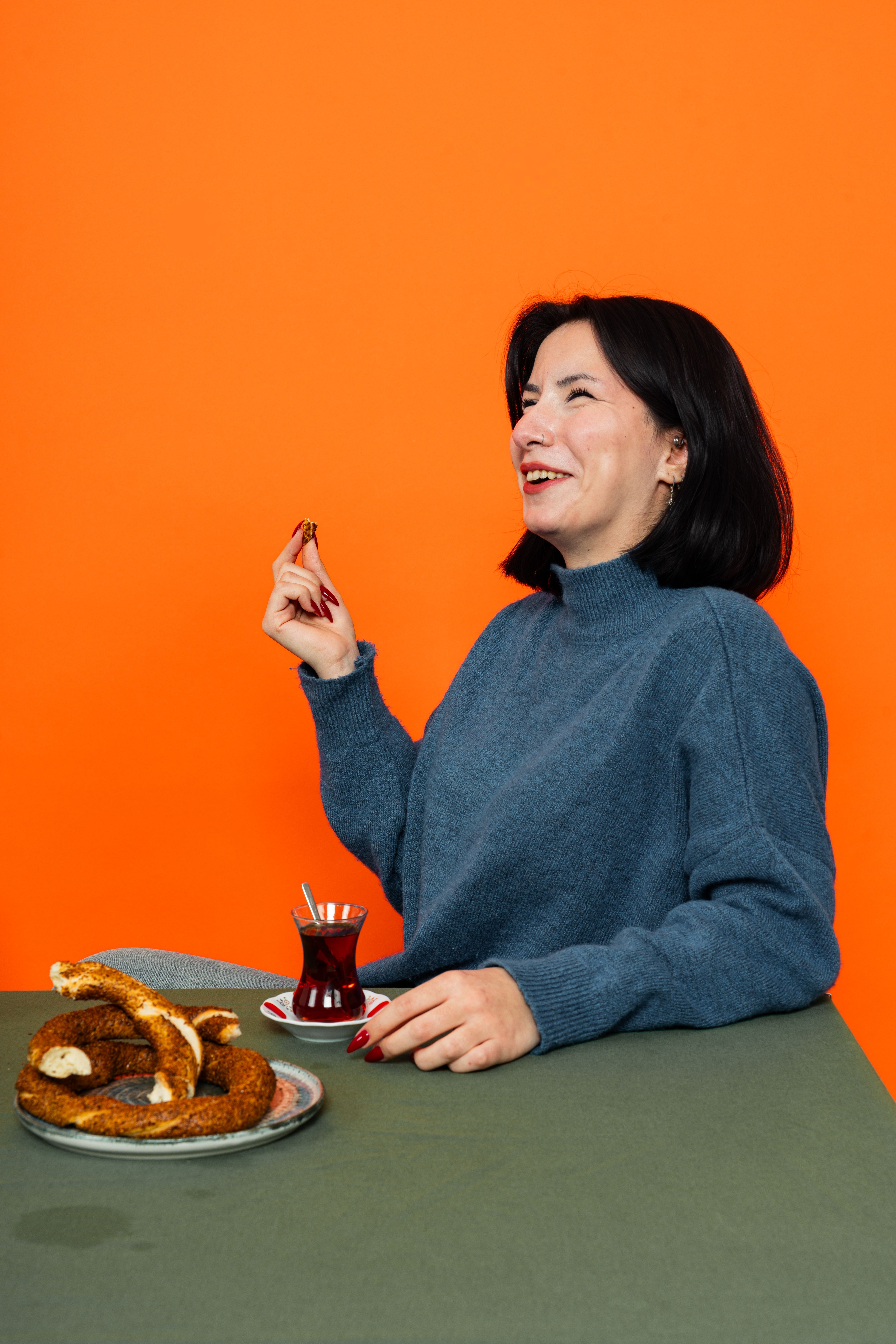 Smiling woman enjoying tea and simit pastry in a vibrant setting. Delightful and colorful moment captured.