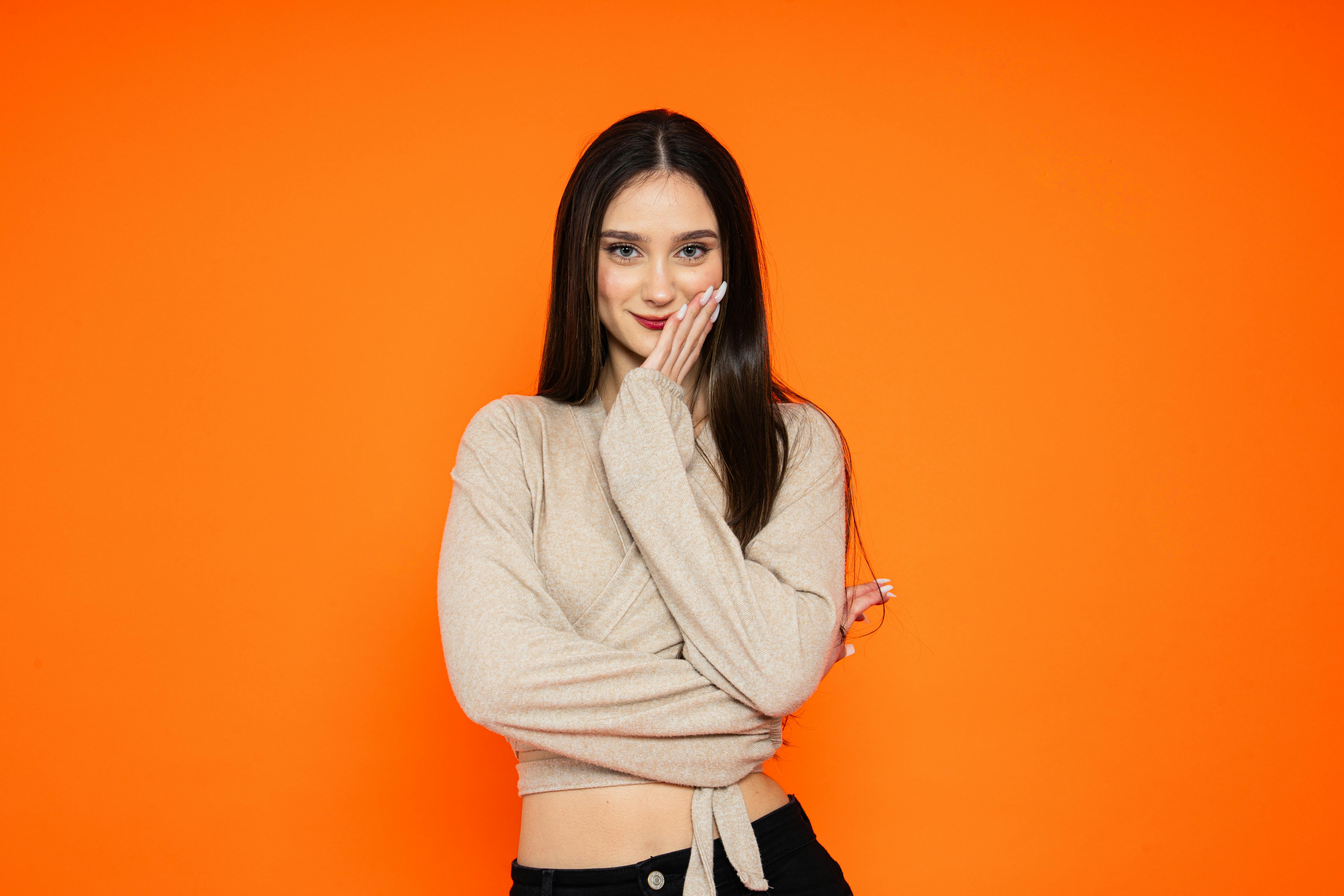 De franc Una dona jove posa amb confiança amb un somriure juganer sobre un fons taronja vibrant. Foto d'estoc