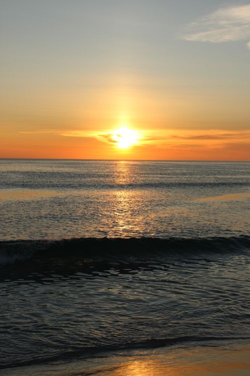 Free Beautiful tropical sunset over ocean waves with a warm glow and serene ambiance. Stock Photo