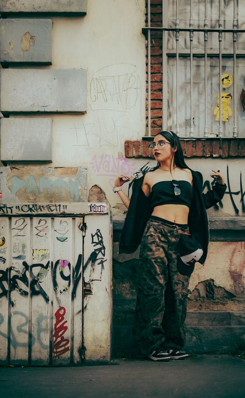 Free A stylish woman poses confidently in front of a graffiti-adorned wall in an urban setting. Stock Photo