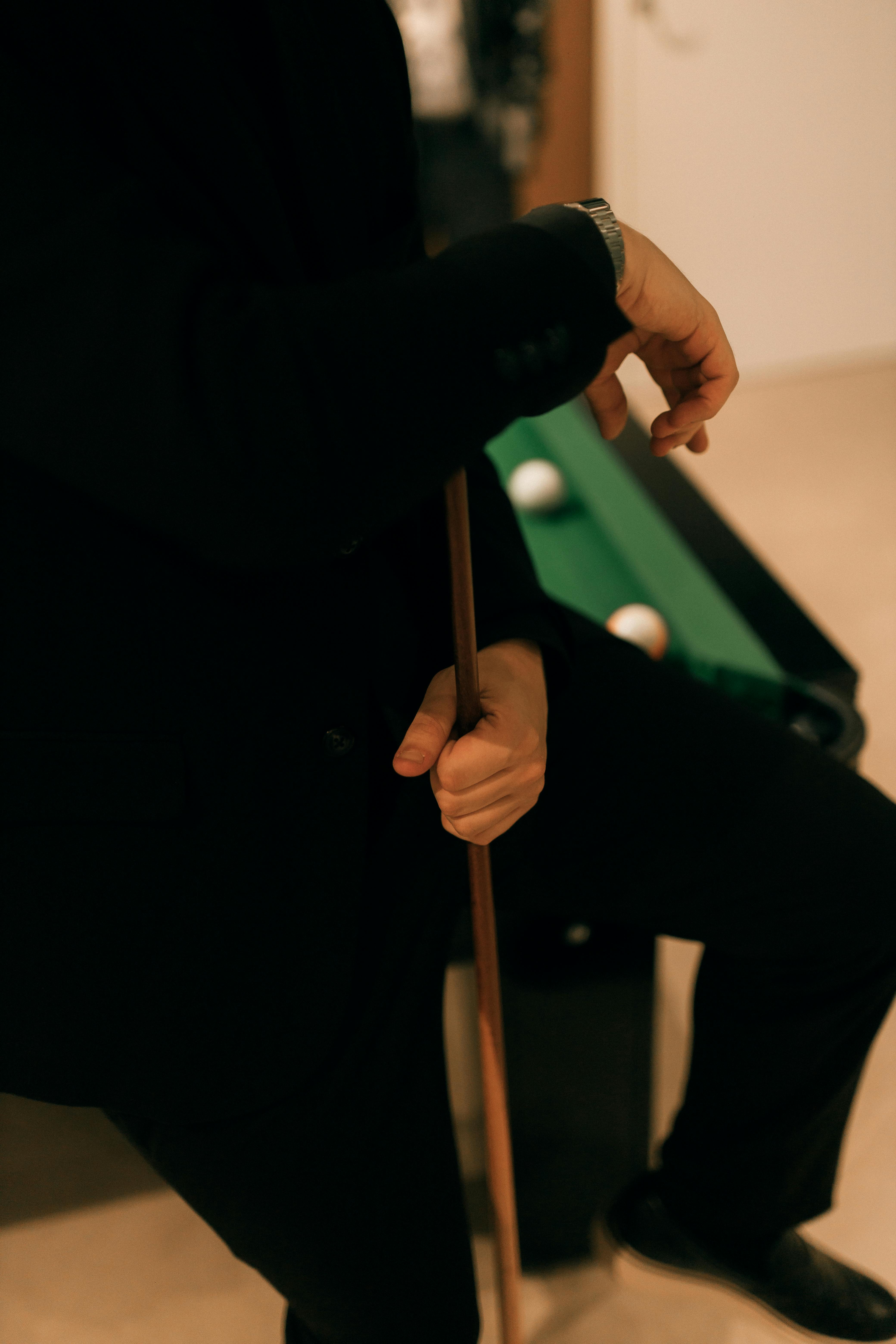 De franc Un home ben vestit sosté un tac de billar, dret al costat d'una taula de billar a l'interior. Foto d'estoc