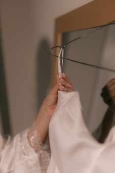 Hands gently hang white fabric on hanger with delicate details in soft lighting.