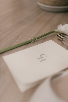 Soft focus flat lay of wedding accessories with rings and a single flower on a wooden surface.