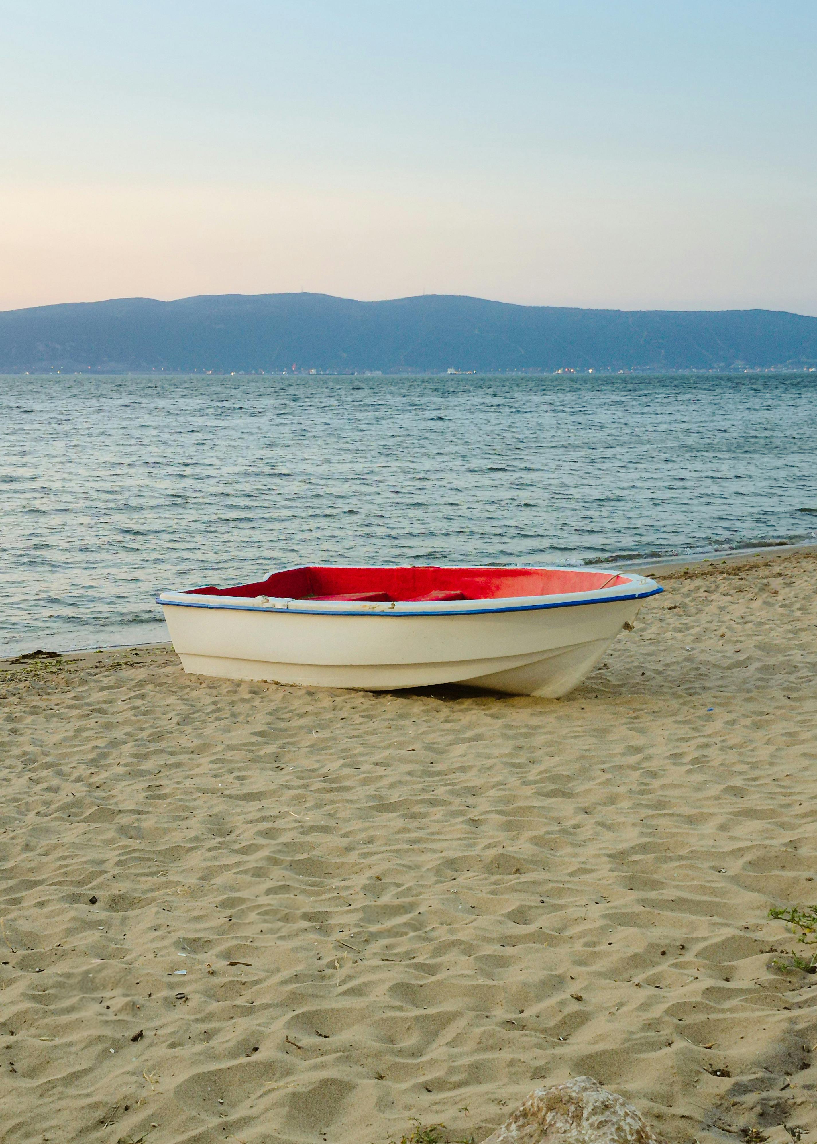 A serene image of a single rowboat on a sandy beach with calm waters and distant hills at twilight.
