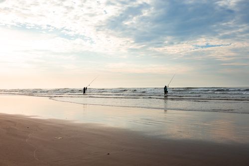 Free Two people fishing at sunrise on a Brazilian beach. Calm ocean waves and a peaceful sky. Stock Photo