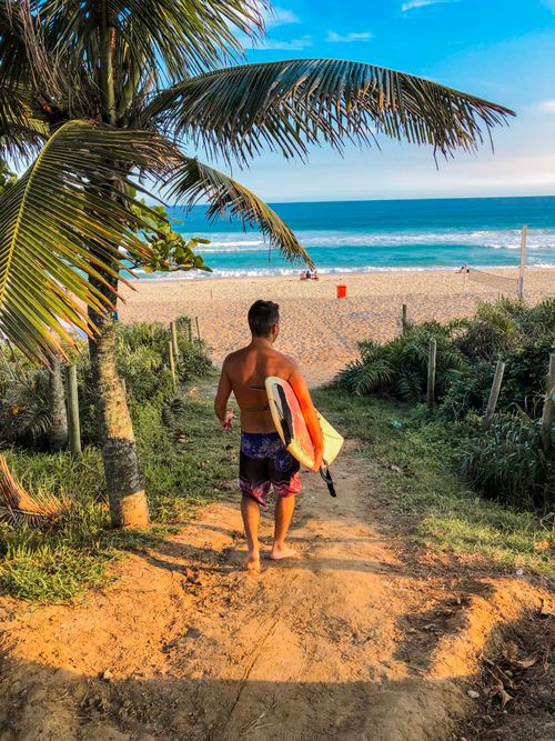 Free Surfer heading to beach with board at tropical sunrise Stock Photo