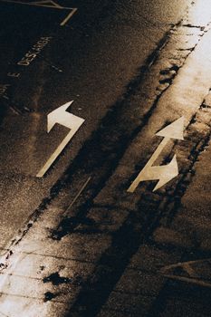 Moody wet street with directional arrows at night, creating an atmospheric urban scene.