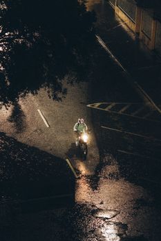 A lone motorcyclist travels on a rainy night, reflecting light on wet pavement.