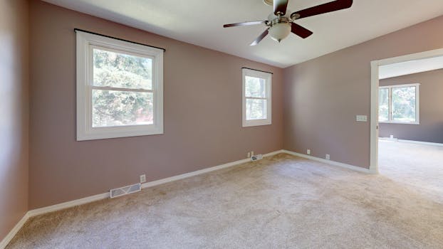 Bright empty room with carpet, windows, and ceiling fan ideal for real estate listings.