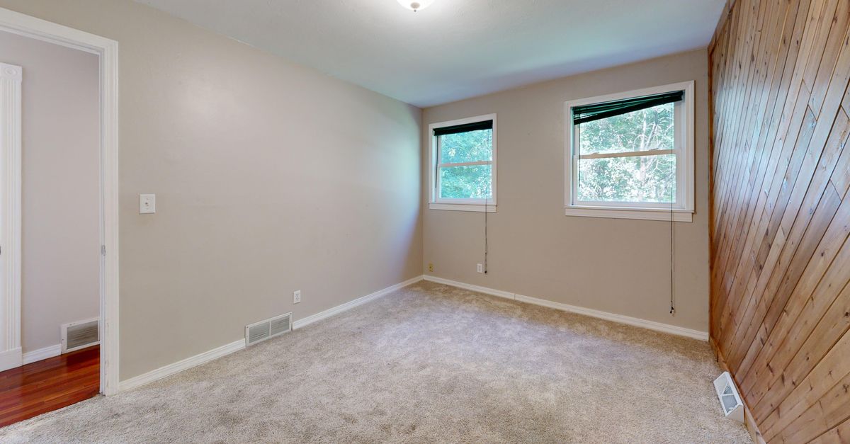 Bright empty room featuring carpet, wooden wall, and two windows.