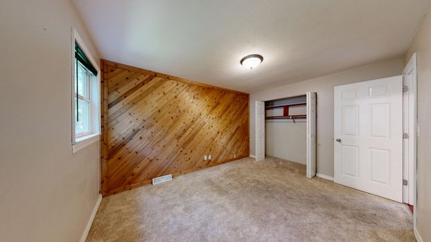 Spacious empty room featuring a wooden accent wall and carpet flooring.