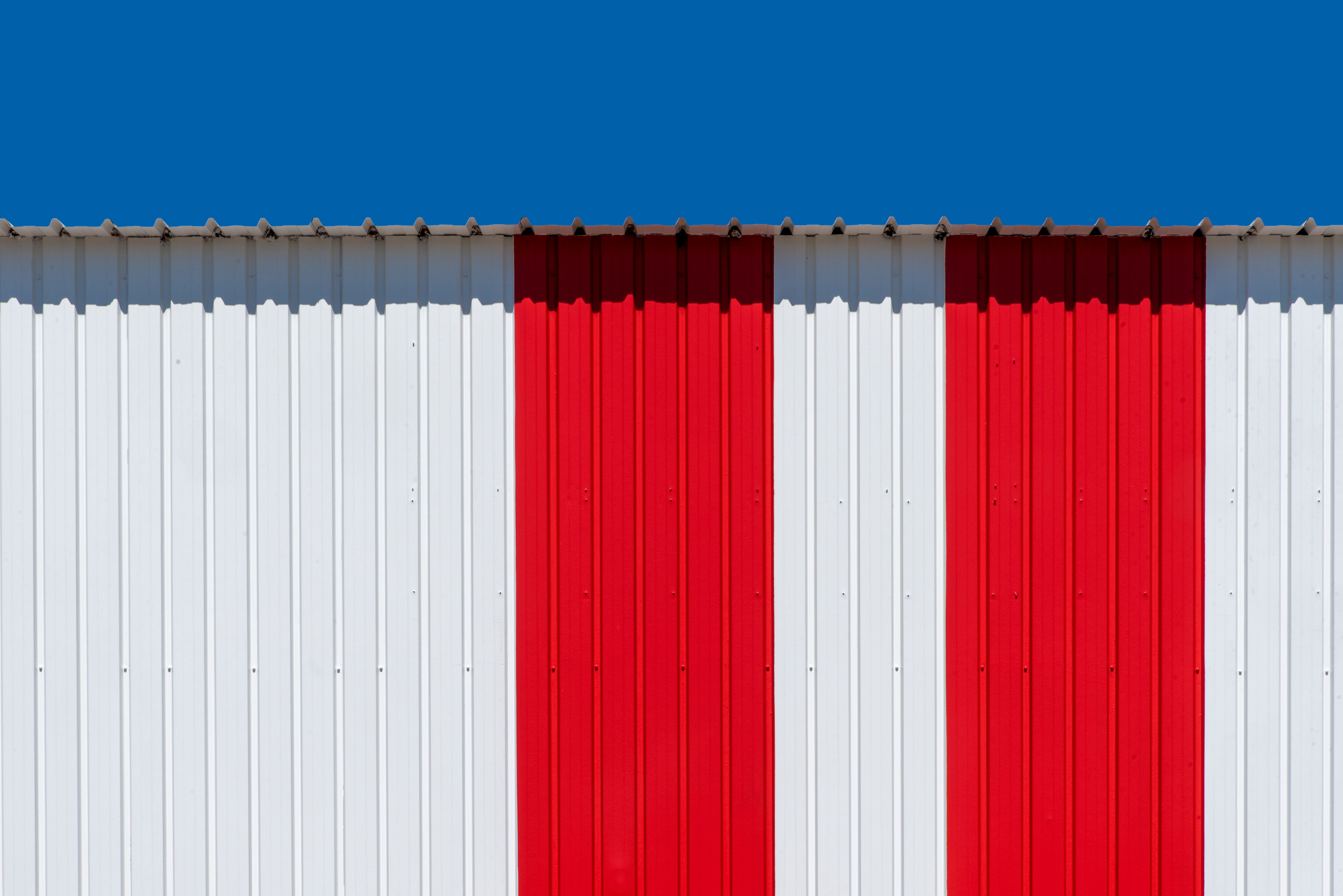 Photo minimaliste d'un mur métallique à rayures rouges et blanches sur fond de ciel bleu vif.