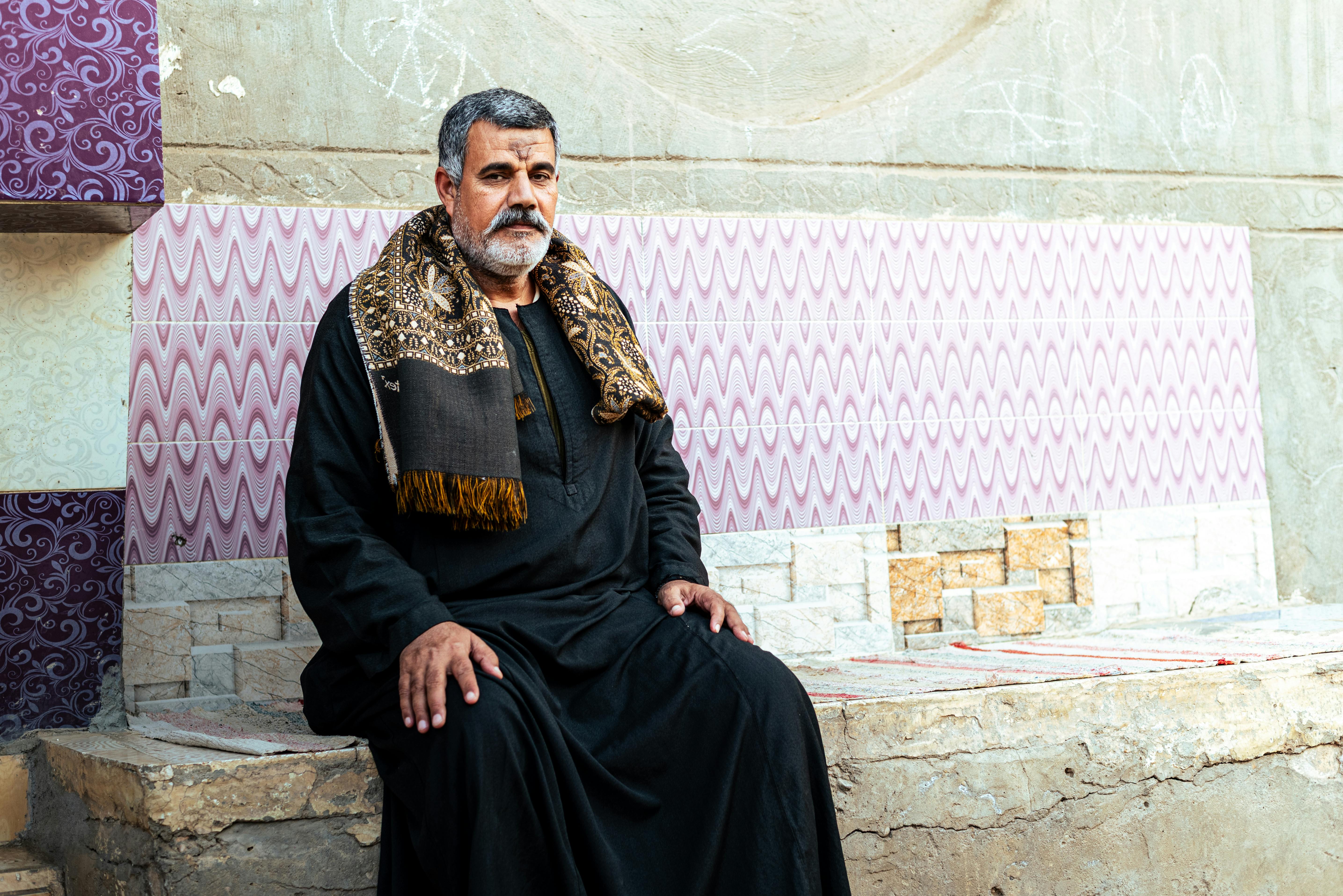 Gratis En kontemplativ mann fra Midtøsten sitter utendørs i tradisjonell antrekk mot en utsmykket vegg i Egypt. Arkivbilde