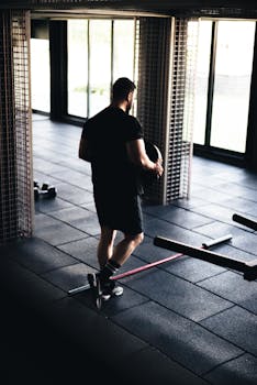 Athletic man working out in a modern gym, holding weights near large windows.