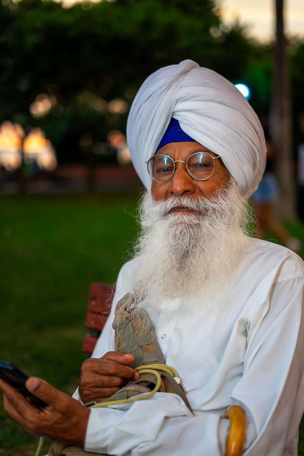 An elderly Sikh man with a beard sitting outdoors in a park