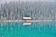 冬日宁静的湖边，一间小屋矗立在结冰的湖岸，周围环绕着白雪覆盖的冷杉