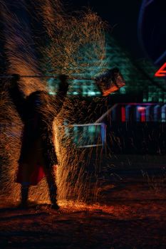 A person swings a fiery tool creating sparks in a vibrant night display.