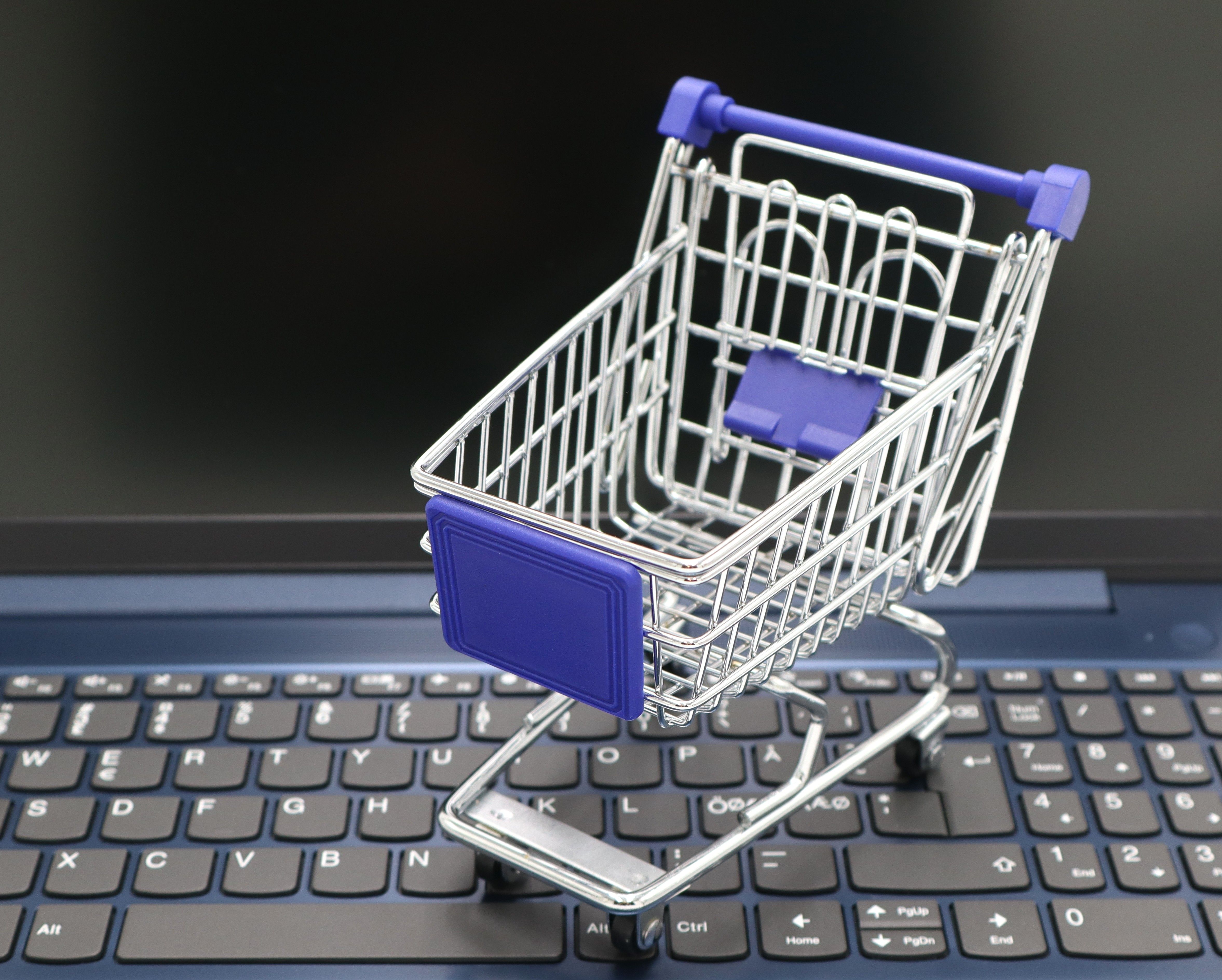 Miniature shopping cart on a laptop representing online commerce