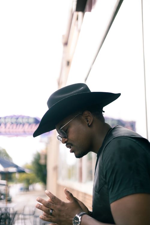 Free Man in a cowboy hat standing outside a building in a reflective pose. Stock Photo