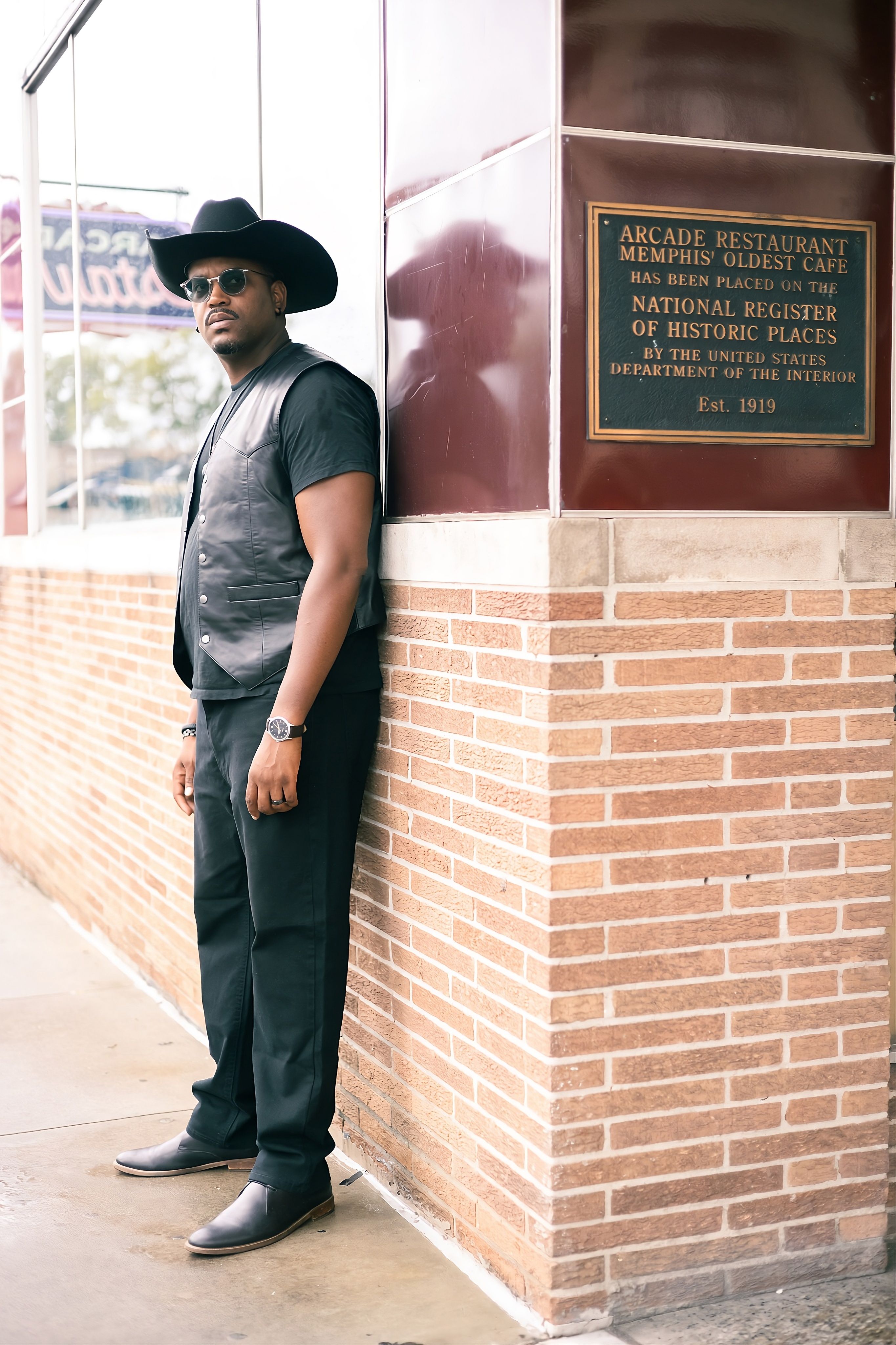 Man in sunglasses and cowboy hat stands by Arcade Restaurant historic plaque, Memphis.