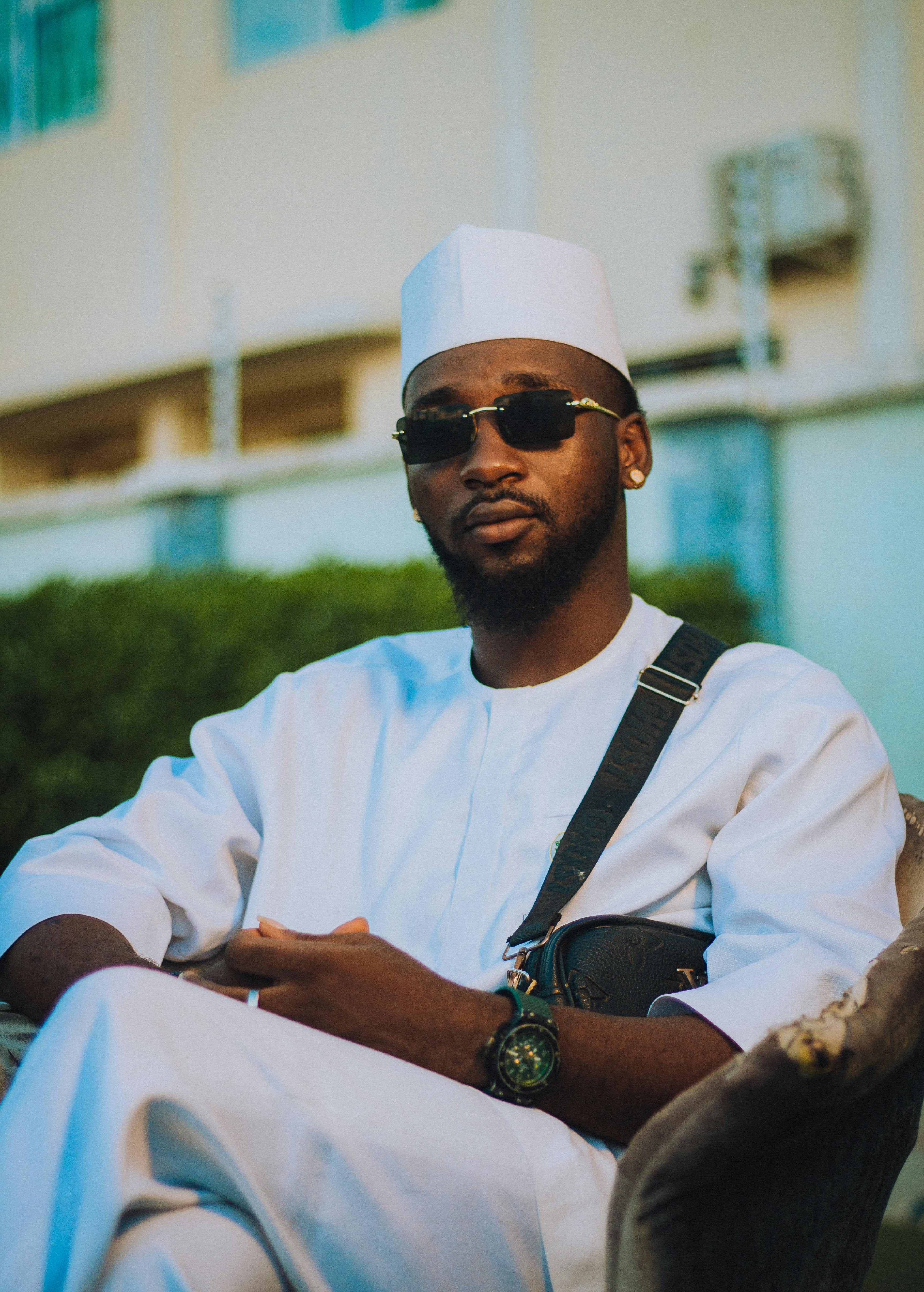 De franc Retrat d'un home amb vestit blanc tradicional i ulleres de sol, assegut a l'aire lliure amb una postura segura. Foto d'estoc