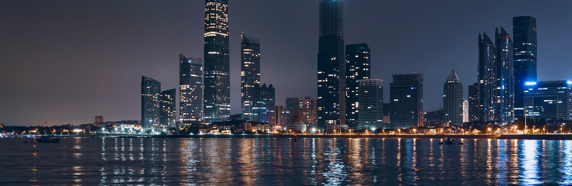 Night view of Abu Dhabi skyline with reflections on water, showcasing modern architecture.