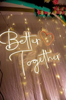 Beautiful neon sign 'Better Together' with heart and floral garland, perfect for wedding decor.