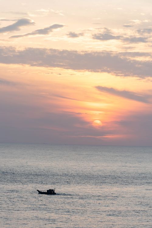 Free Serene sunset over the sea in Vũng Tàu, Vietnam, with a silhouette of a lone fishing boat. Stock Photo