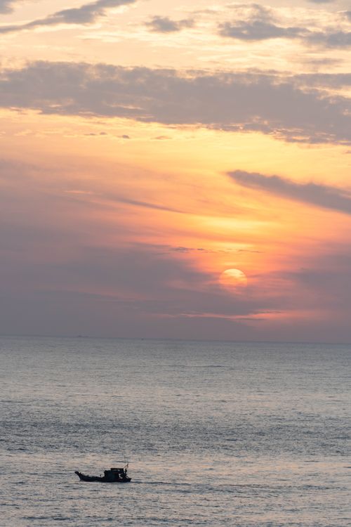 Free A tranquil sunset over the ocean with a lone fishing boat in Vũng Tàu, Vietnam. Stock Photo