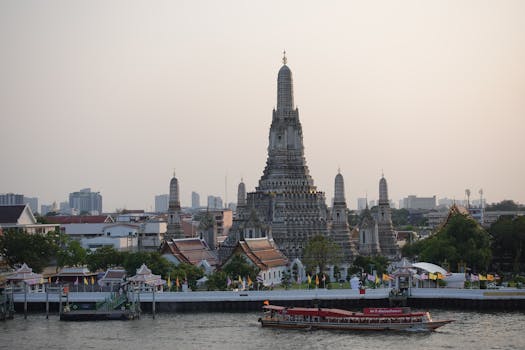 A stunning view of Wat Arun temple in Bangkok with a river scene at sunset, showcasing Thai architecture.
