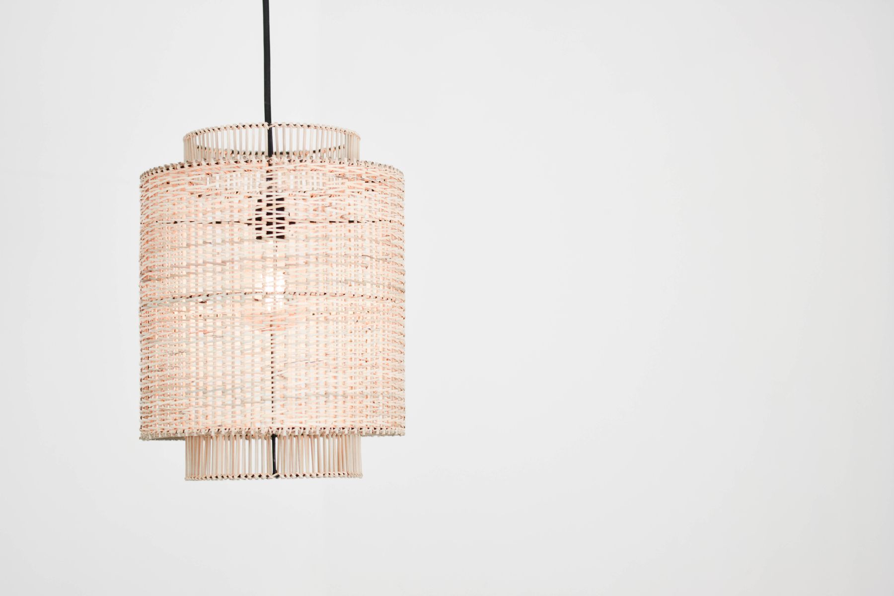 Cylindrical woven pendant shade suspended against a pale wall