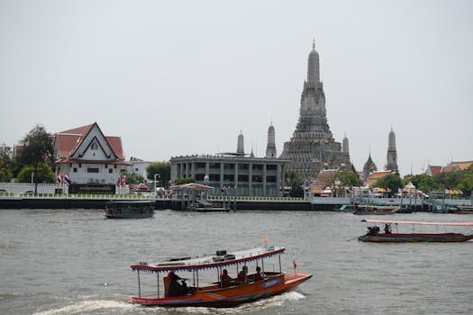 Boats navigating the Chao Phraya River with the iconic Wat Arun temple in Bangkok, Thailand visible in the background.