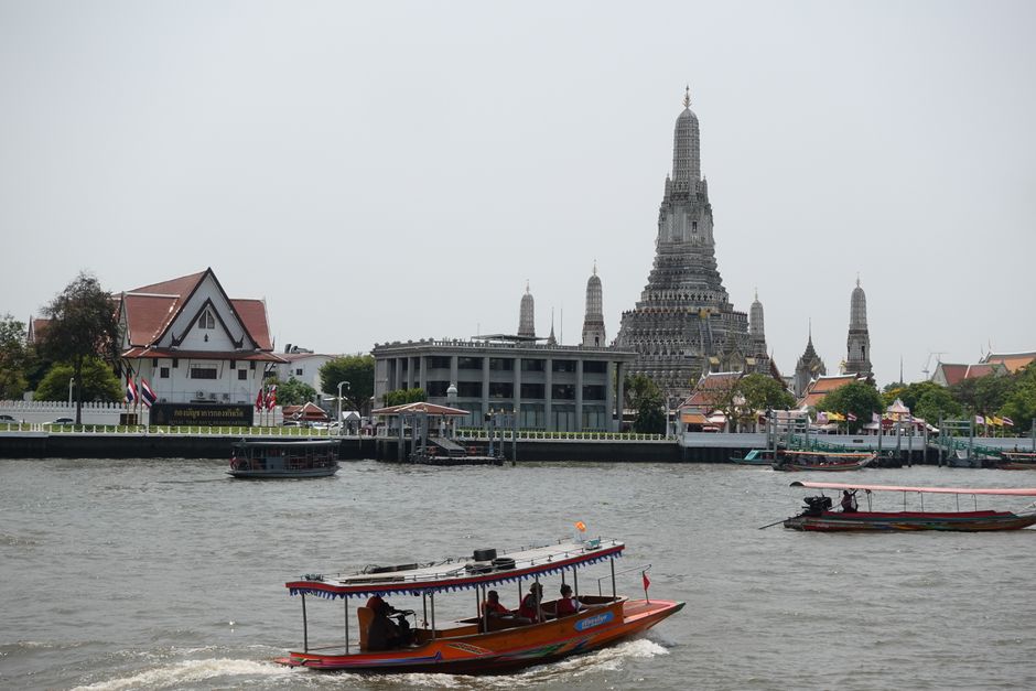 Boats navigating the Chao Phraya River with the iconic Wat Arun temple in Bangkok, Thailand visible in the background.