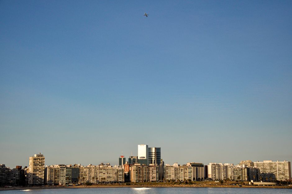 Aerial view of Montevideo's coastal skyline with clear blue sky and airplane flying above.