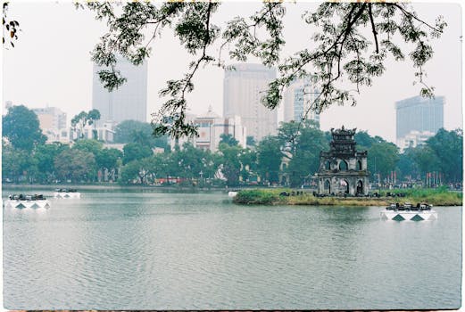 Scenic view of Hoàn Kiếm Lake with Turtle Tower and Hanoi cityscape in the background.