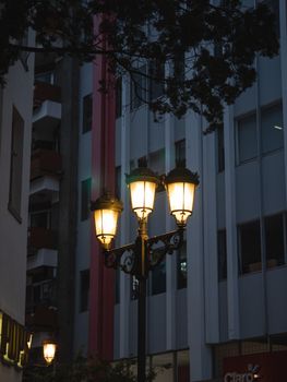 Vintage street lamp glowing at twilight against a cityscape backdrop.
