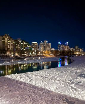 Stunning view of Calgary's skyline at night with river reflections and snow-covered banks.