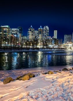 Stunning night cityscape of Calgary skyline reflecting on a snowy riverbank.