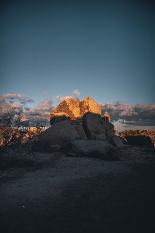 Free Sunset highlights rugged rock formation in a remote desert landscape with dramatic sky. Stock Photo