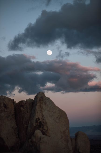 Full moon illuminates rocky formations under a dramatic twilight sky in the California desert.